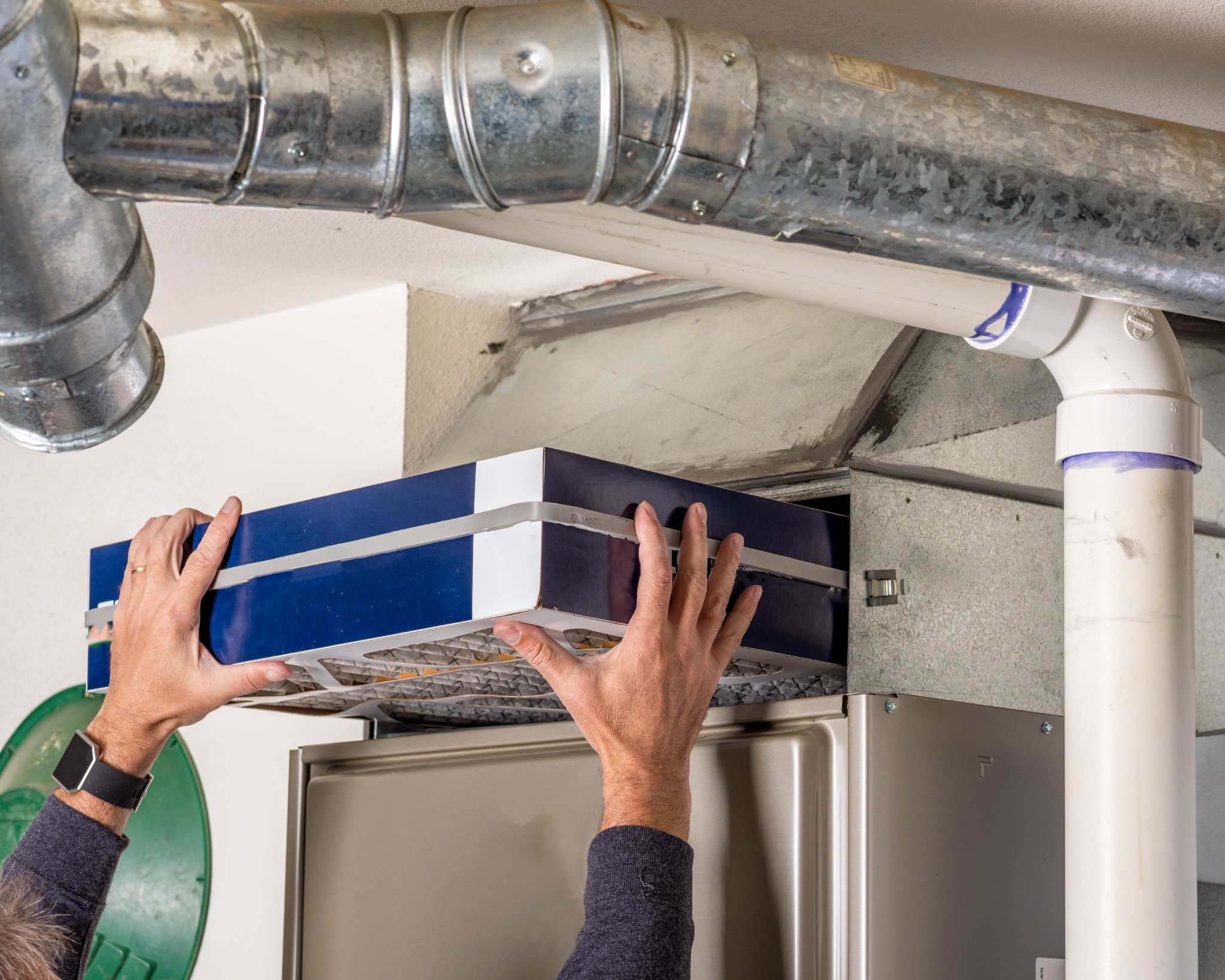 A person performs a furnace filter replacement by sliding a new air filter into a home HVAC system to improve air quality and efficiency.