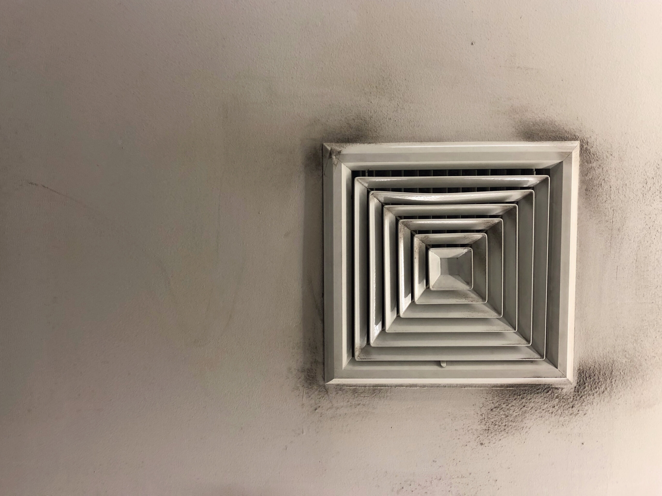 Air vent on a ceiling with visible mold and dark stains around the grille, indicating possible HVAC mold contamination.